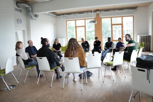 A group of people sit in a circle of chairs and talk.