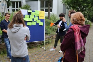 (Foto: UW/H | Kay Gropp) Es sind Menschen zu sehen, die an einer Tafel gemeinsam an einer Strategie arbeiten
