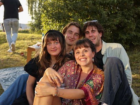 Eine Gruppe von vier Studierenden sitzt im Schatten auf einer Wiese.