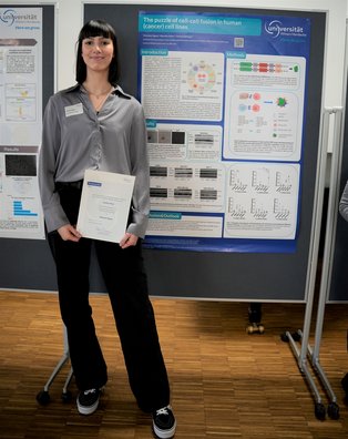 Vivienne Ogasa Eine Frau mit einer Urkunde in der Hand steht vor einer Stellwand mit einem Poster.