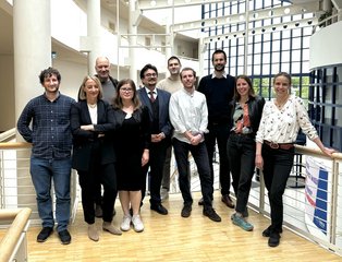 A GROUP of 10 people stand up in a building and smile at the camera.