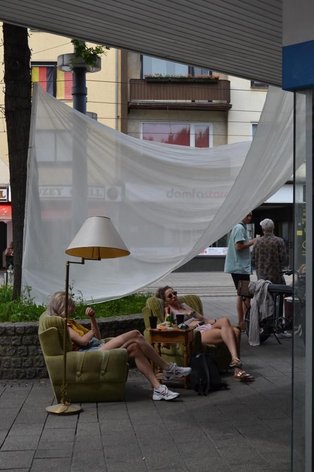 Two young women hang out on armchairs on the sidewalk.
