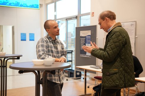 Two men are standing at a bar table and talking to each other.