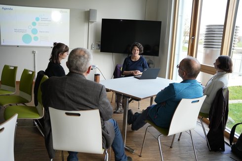 Five people sit around a table and talk.